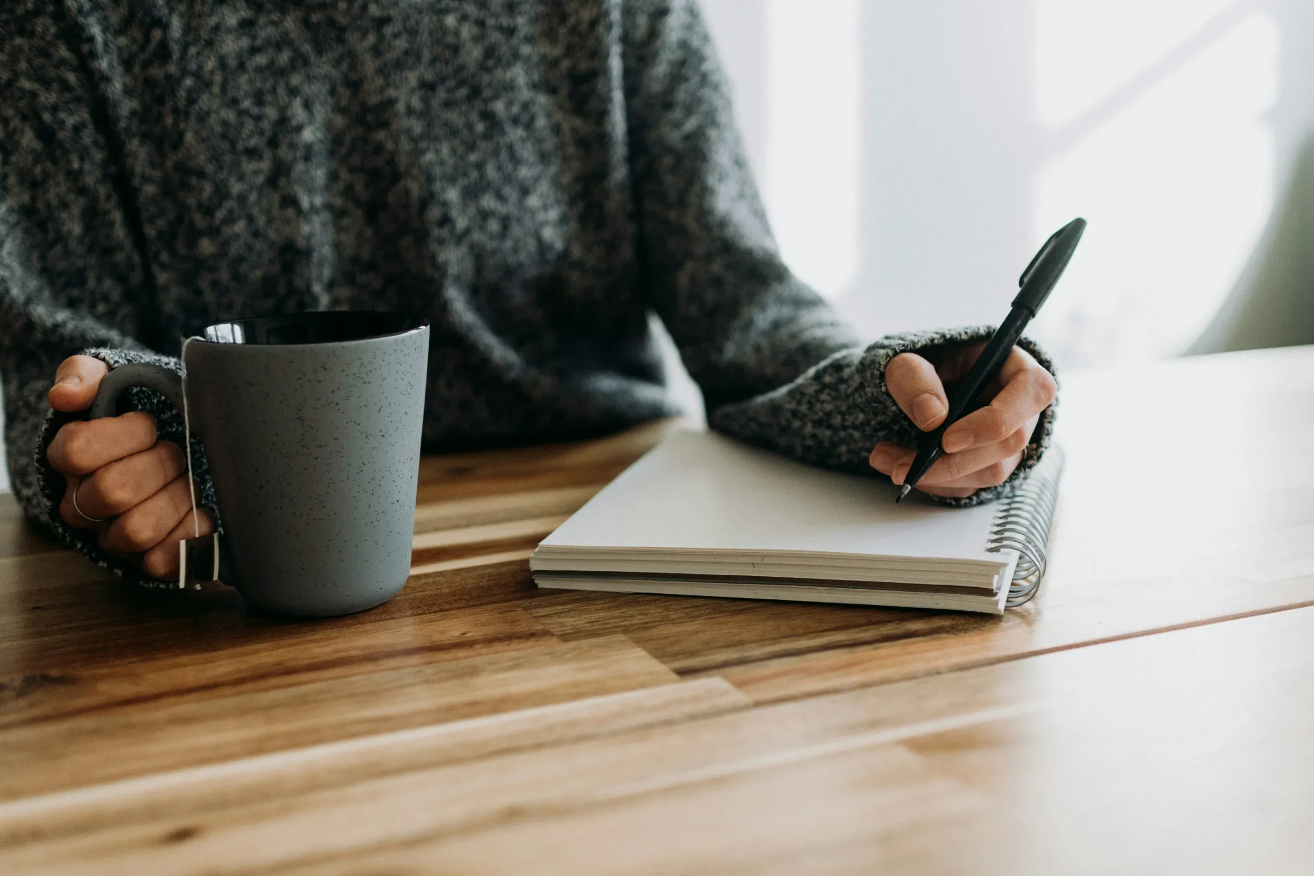 Hands holding a warm mug, a notebook open on a blanket in evening lamp light